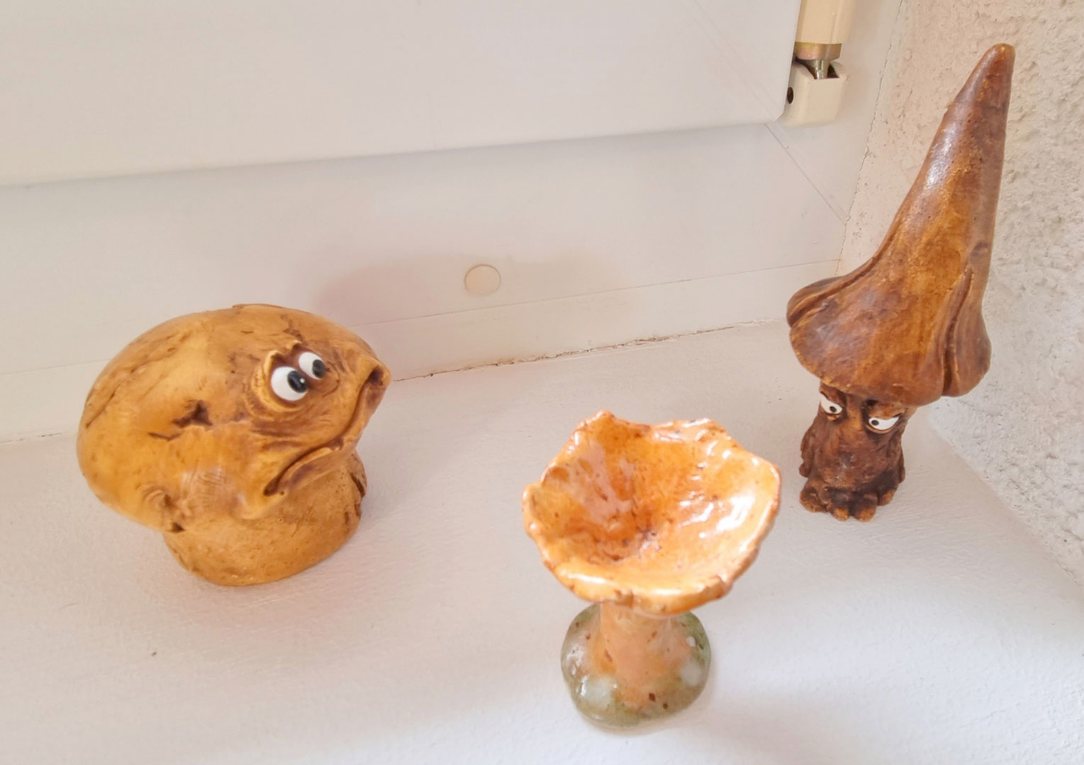 deux champignons avec des yeux en résine regardent une chanterelle en terre cuite (sans yeux) au centre