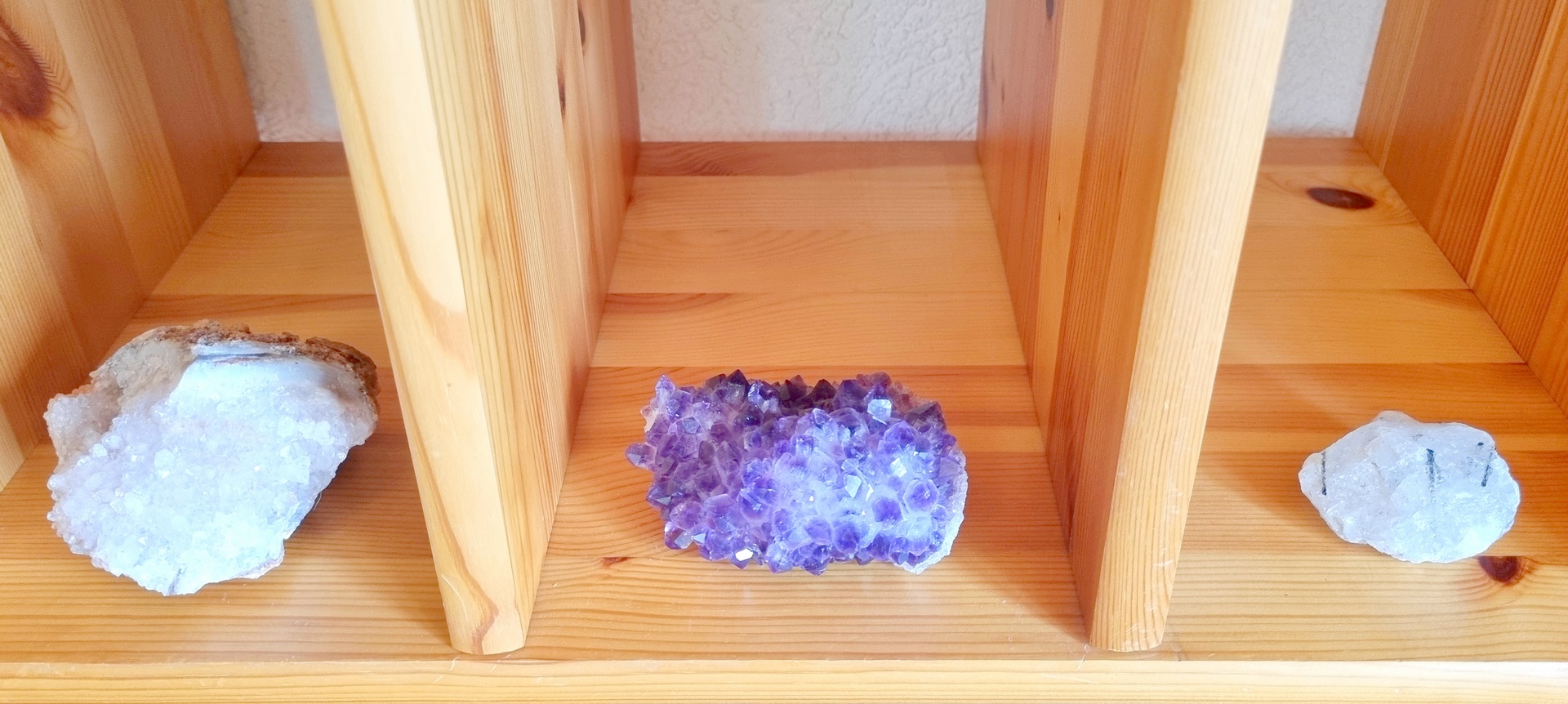 trois pierres dans une étagère, une pierre avec plein de petit cristaux de quartz à gauche, une améthyste au centre, une tourmaline en quartz à droite