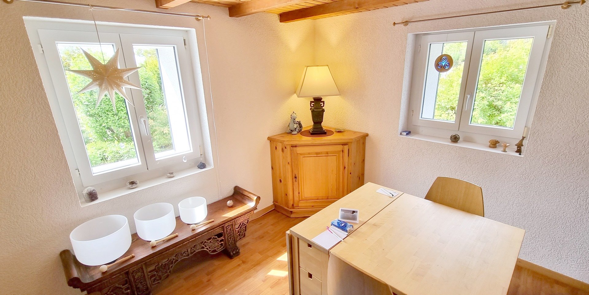 fenêtre à droite, meuble bas avec bols en cristal sous la fenêtre, meuble d&apos;angle au centre avec une lampe à pied, fenêtre à gauche, une table et chaise au centre droit 